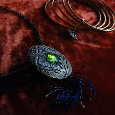 Vintage ornate flourish brass button with green cabochon rhinestone. Blue fringe tassel. 