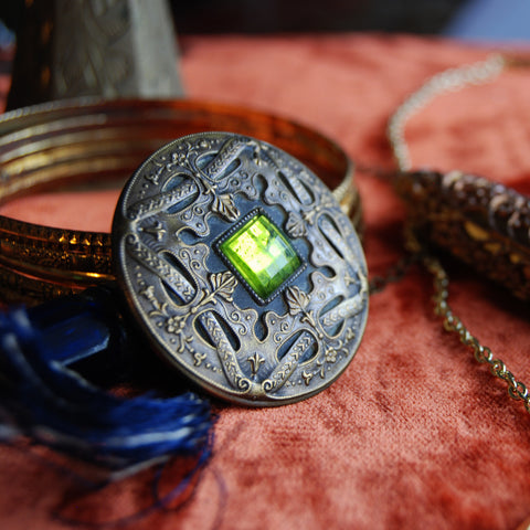 Vintage ornate flourish brass button with green cabochon rhinestone. Blue fringe tassel. 