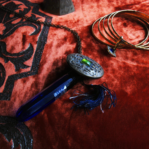 Vintage An Evening in Paris cobalt blue glass perfume bottle. Brass chain necklace with fringe tassel. Vintage ornate button.